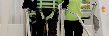 Therapeutin unterstützt Patienten auf dem Gangtrainer