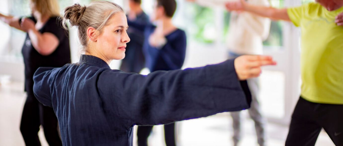 Therapeutin und Patientengruppe beim gemeinsamen Tai-Chi in der Sporthalle