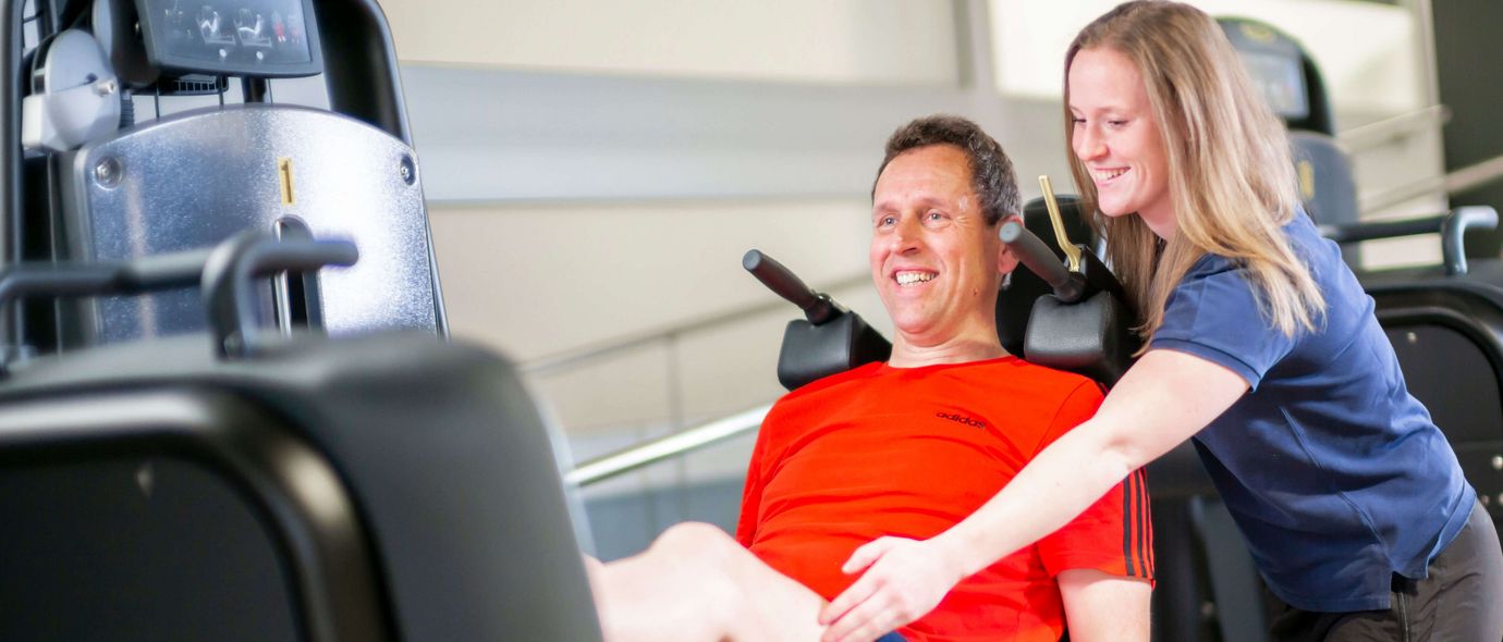 Therapeutin erklärt Patienten, wie die Beinpresse funktioniert