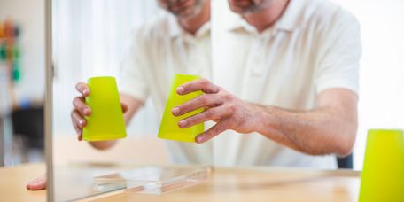 Patient hebt Ball mit der Hand vor dem Spiegel