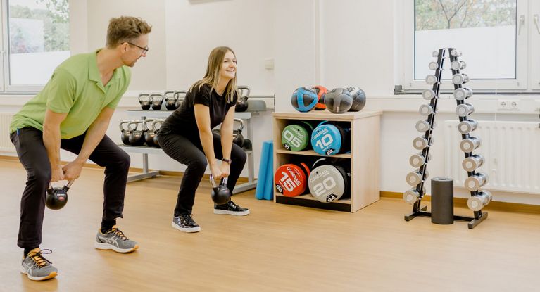 Therapeutin und Patient trainieren mit kleinen Gewichten