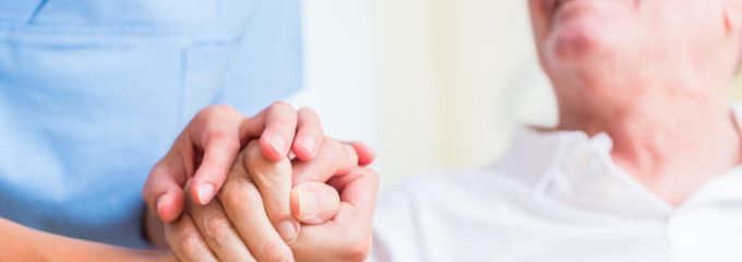 Pflegerin hält die Hand eines älteren Patienten