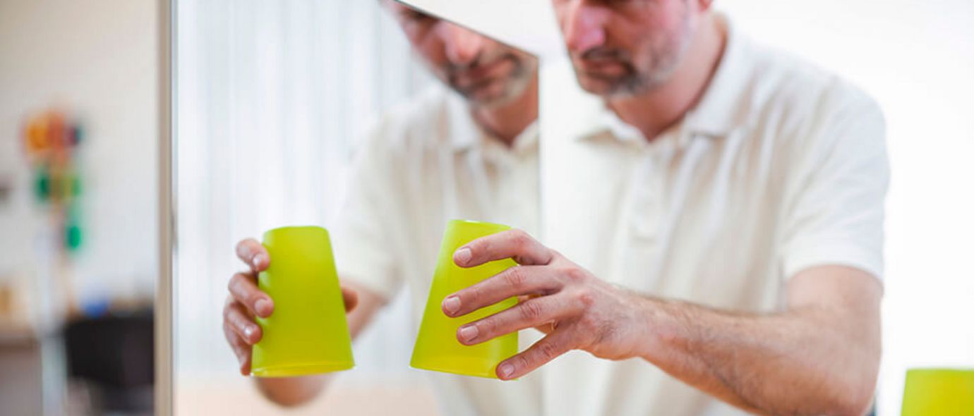 Patientin hält Glas vor Spiegel bei Spiegeltherapie
