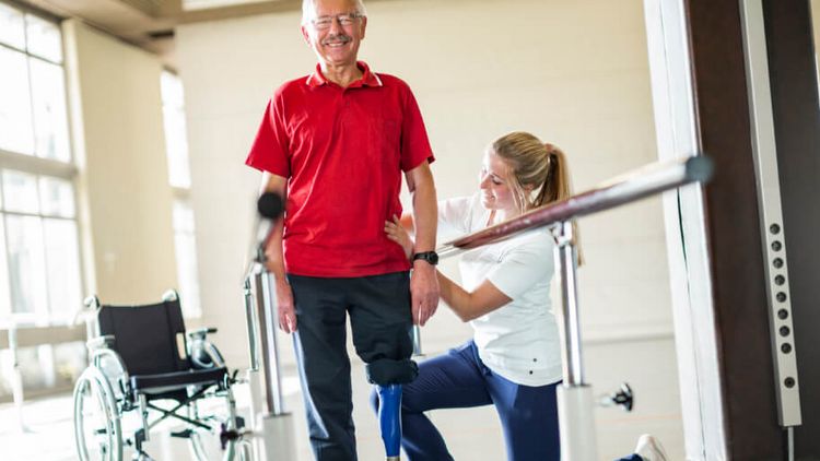 In der Gehschule unertstützt eine Therapeutin einen beinamputierten Patient beim Laufen mit der Prothese
