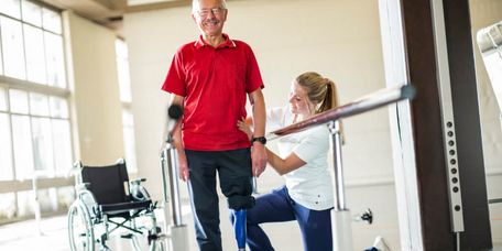 In der Gehschule unertstützt eine Therapeutin einen beinamputierten Patient beim Laufen mit der Prothese