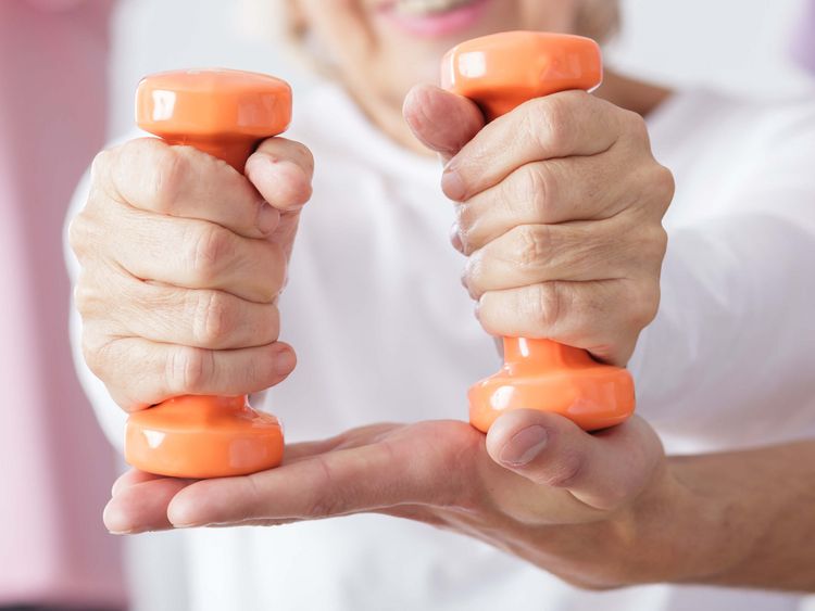 Eine Seniorin trainiert mit kleinen orangefarbenen Gewichten