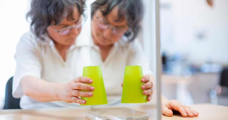 Patientin hält Becher vor einen Spiegel